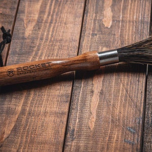 May include: A wooden brush with black bristles and a leather strap. The handle is engraved with the words "ROCKET ESPRESSO MILANO".