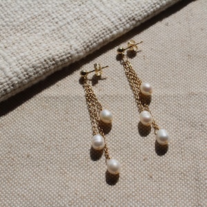 May include: A pair of gold dangle earrings with three white pearls on each earring.