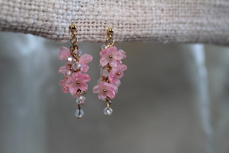 May include: A pair of dangle earrings with pink flower-shaped beads and clear crystal beads hanging from gold-toned posts.