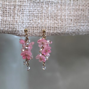 May include: A pair of delicate earrings featuring pink flower-shaped charms dangling from gold-toned posts. The charms are arranged in a cascading design, creating a whimsical and feminine look.