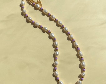 May include: A gold chain necklace with white pearls and lavender beads.