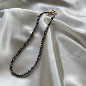 May include: A black pearl necklace with a gold clasp. The necklace is made of small, irregular pearls.