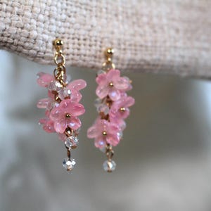 May include: Pink flower-shaped earrings with gold accents and crystal beads hanging from the bottom.