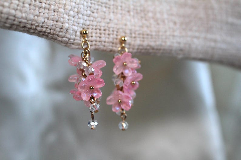 May include: Pink flower-shaped earrings with gold accents and crystal beads hanging from the bottom.