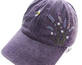 May include: A purple baseball cap with embroidered lavender flowers and a bee. The cap has a curved brim and a mesh back.