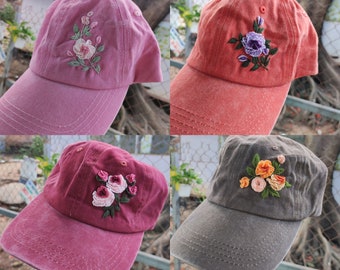May include: Four embroidered baseball caps with floral designs. The caps are in pink, red, grey, and burgundy. Each cap has a different floral design embroidered on the front.