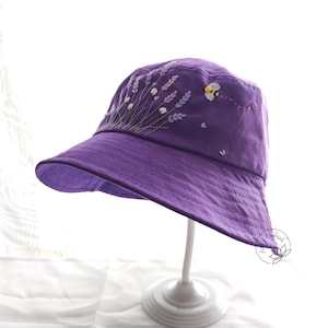 Peut inclure: Chapeau bob en tissu violet avec des fleurs de lavande brodées et un motif d'abeille.