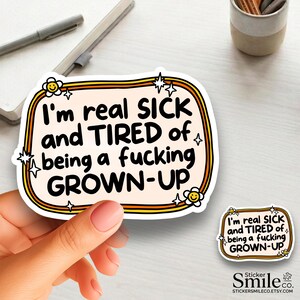 May include: A rectangular sticker with rounded corners featuring a cream background, orange and brown border lines, and two small smiling flower icons. The black text reads: I'm real SICK and TIRED of being a fucking GROWN-UP, accented by small star shapes.