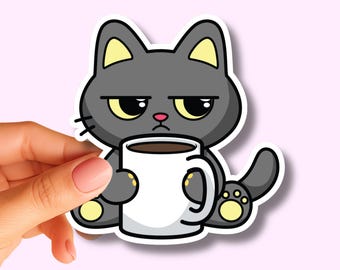May include: A die-cut vinyl sticker featuring a grumpy grey cartoon cat with yellow inner ears and paw pads, holding a large white mug filled with dark coffee. The cat has a small pink nose and a stern expression. The text Sticker Smile co. is visible.