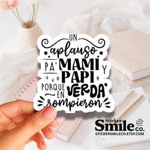 May include: A white sticker with black text that reads "Un aplauso pa' Mami y Papi porque en verda' rompieron." The sticker also features the Sticker Smile Co. logo and website address.