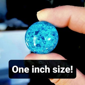K&ouml;nnte beinhalten: Eine blaue Glaskugel mit einem Durchmesser von 2,5 cm und einem funkelnden, irisierenden Finish.