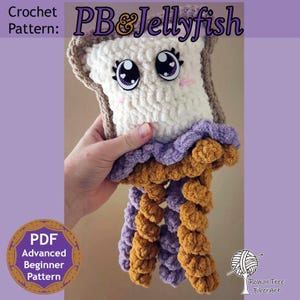 May include: A plush crochet toy shaped like a slice of bread with a brown crust and white center, featuring large cartoon eyes and pink cheeks. Below the bread are dangling tentacles in purple and golden brown yarn. Text reads PB&Jellyfish.