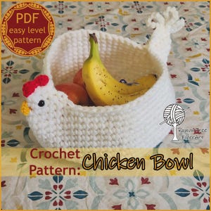 May include: A white crochet chicken bowl filled with bananas and oranges. The bowl has a red comb and yellow beak. The text "Crochet Pattern: Chicken Bowl" is visible. The bowl is handmade and perfect for kitchen decor.