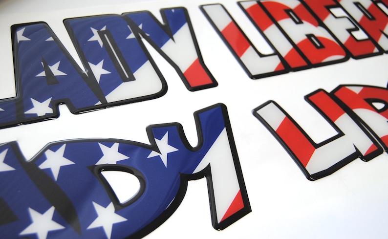 Puede incluir: Tres pegatinas de vinilo en relieve con un dise&ntilde;o de bandera estadounidense. Las pegatinas deletrean "LADY LIBERTY".
