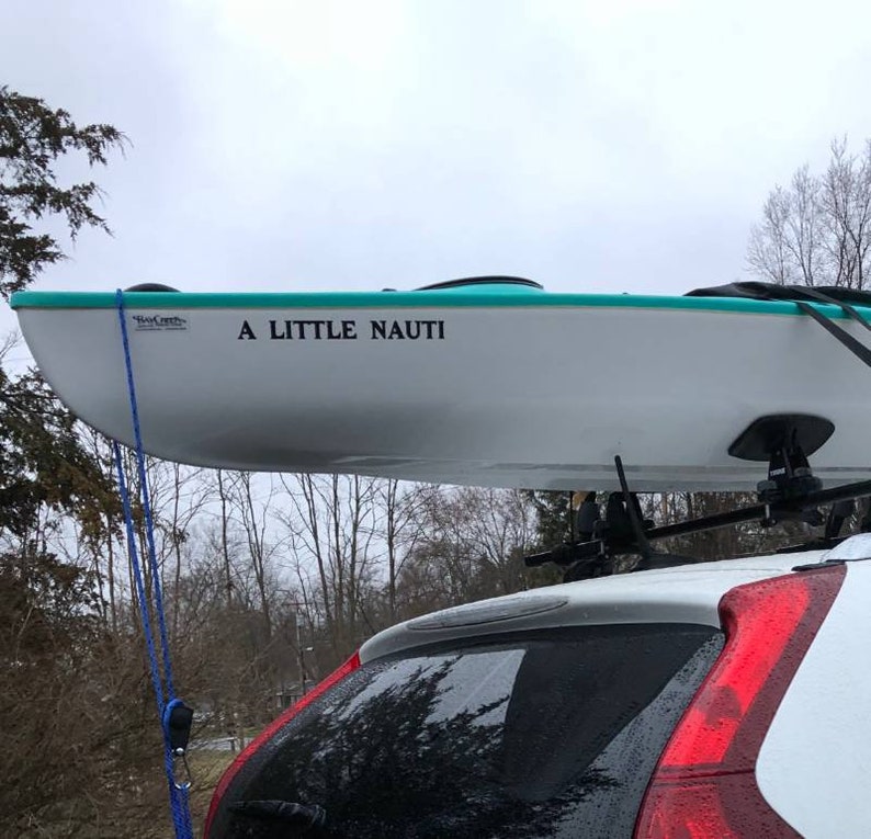 K&ouml;nnte beinhalten: Ein wei&szlig;es Kajak mit t&uuml;rkisfarbenem Rand ist auf dem Dach eines wei&szlig;en Autos befestigt. Das Kajak hat einen schwarzen Aufkleber mit der Aufschrift "A LITTLE NAUTI".