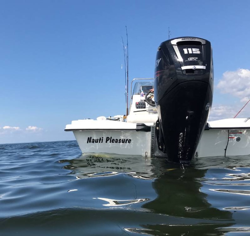 K&ouml;nnte beinhalten: Ein wei&szlig;es Boot mit einem schwarzen Au&szlig;enbordmotor mit der Aufschrift "Mercury 115" befindet sich im Wasser. Das Boot hat einen schwarzen Aufkleber mit der Aufschrift "Nauti Pleasure" an der Seite.