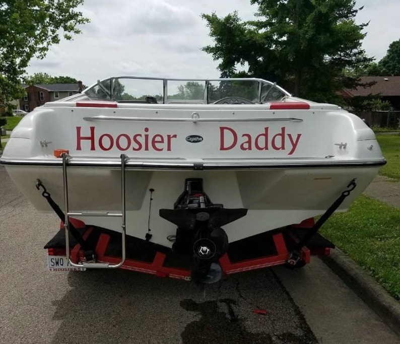 K&ouml;nnte beinhalten: Ein wei&szlig;es Boot mit der Aufschrift "Hoosier Daddy" in Rot auf der R&uuml;ckseite. Das Boot steht auf einem Anh&auml;nger mit einer Leiter an der Seite.