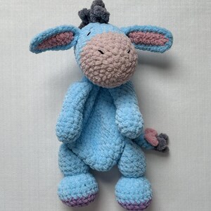 May include: A handmade plush donkey toy in shades of blue, pink, and gray. The donkey has large ears with pink inner ears, a pink muzzle, and a gray tuft of hair. The plush toy is soft and cuddly, perfect for a child's bedroom or nursery.