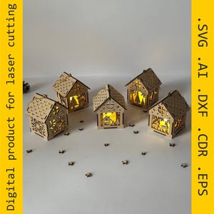 May include: Five small, wooden house-shaped lanterns with intricate cut-out designs. Each lantern has a warm, yellow light inside, creating a cozy glow. The houses are decorated with stars and snowflakes. The image also includes the text "Digital product for laser cutting".