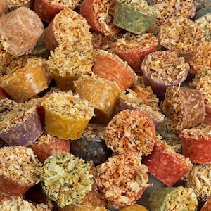 May include: A close-up of a variety of colorful dog treats. The treats are shaped like small cups and are filled with a mixture of shredded ingredients. The treats are a mix of orange, red, green, and brown.