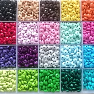 Könnte beinhalten: Eine transparente Plastik-Aufbewahrungsbox gefüllt mit kleinen, runden Holzperlen in verschiedenen Farben, darunter Weiß, Schwarz, Rot, Rosa, Lila, Grau, Blau, Grün und Türkis.