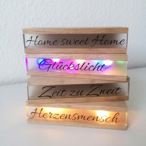 Könnte beinhalten: Vier Holzblöcke mit klaren Glasplatten und LED-Lichtern. Die Blöcke sind übereinander gestapelt. Der oberste Block lautet "Home sweet Home". Der zweite Block lautet "Glückslicht". Der dritte Block lautet "Zeit zu Zweit". Der unterste Block lautet "Herzensmensch".