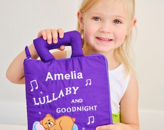 May include: A purple fabric book with a handle, featuring the text "Amelia Lullaby and Goodnight" with a musical note and a sleeping bear illustration.