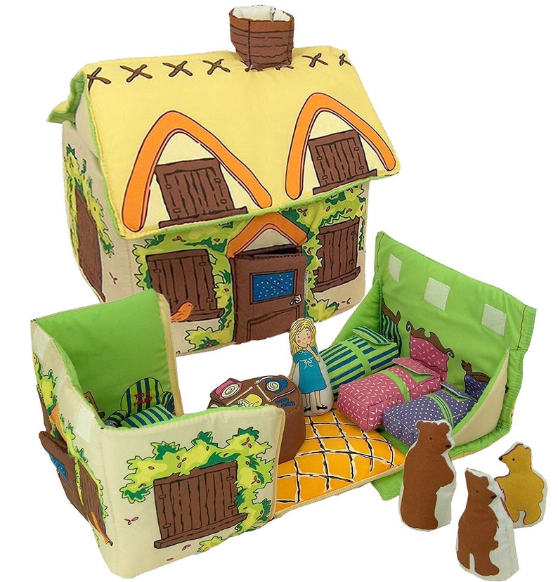 May include: A soft toy house with a yellow thatched roof, brown shutters, and green foliage. The house opens to reveal a bedroom with three beds, a doll, and three bear figures. The toy is designed for children.