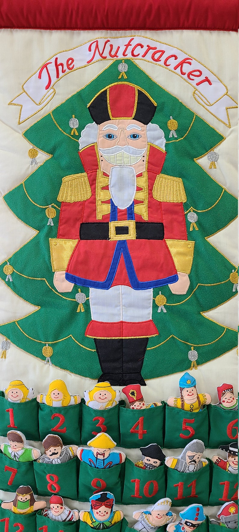 May include: A green felt advent calendar with a Nutcracker theme. The calendar features a large embroidered Nutcracker figure standing in front of a green Christmas tree. There are 13 pockets on the calendar, each with a different character from the Nutcracker story. The pockets are numbered 1 through 13.