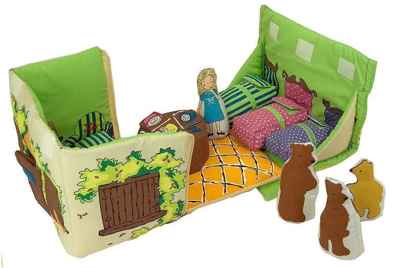 May include: A fabric playset depicting a house interior with a doll and bear figures. The set features green, yellow, and brown colours, with printed details of furniture and a window. Includes three beds, a doll, and three bear figures.