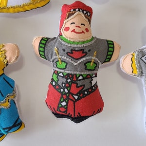 May include: Five handmade felt dolls with embroidered details. The dolls are dressed in different colourful outfits. One doll is wearing a blue and yellow dress with a white hat, another is wearing a red and green dress with a white hat, another is wearing a grey suit with a white shirt and a brown moustache, another is wearing a white dress with gold trim, and another is wearing a blue dress with a white hat.