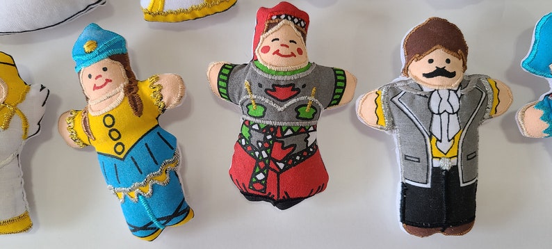 May include: Five handmade felt dolls with embroidered details. The dolls are dressed in different colourful outfits. One doll is wearing a blue and yellow dress with a white hat, another is wearing a red and green dress with a white hat, another is wearing a grey suit with a white shirt and a brown moustache, another is wearing a white dress with gold trim, and another is wearing a blue dress with a white hat.