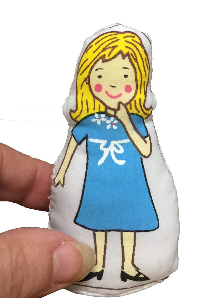 May include: A handmade fabric doll featuring a cartoon girl illustration. The doll has yellow hair, pink cheeks, and wears a blue dress with a white floral design and a white bow. The doll is approximately 10 cm tall.