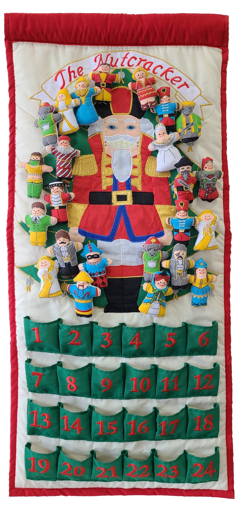 May include: A white fabric advent calendar with a red border and green pockets. The calendar features an embroidered image of the Nutcracker and characters from the ballet. The pockets are numbered 1 through 24.