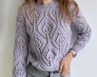 May include: A light purple knitted sweater with a delicate openwork pattern. The sweater has long sleeves and a round neckline.