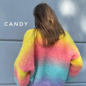 May include: A rainbow ombre knit sweater with a fluffy texture. The sweater is yellow, orange, pink, blue, and purple.