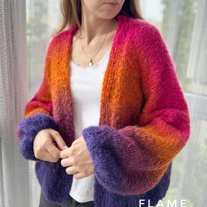 Puede incluir: Un c&aacute;rdigan de manga larga con un degradado de rosa, naranja y morado. El c&aacute;rdigan tiene un corte holgado y cuello en V. El texto "FLAME" es visible en la esquina inferior derecha de la imagen.