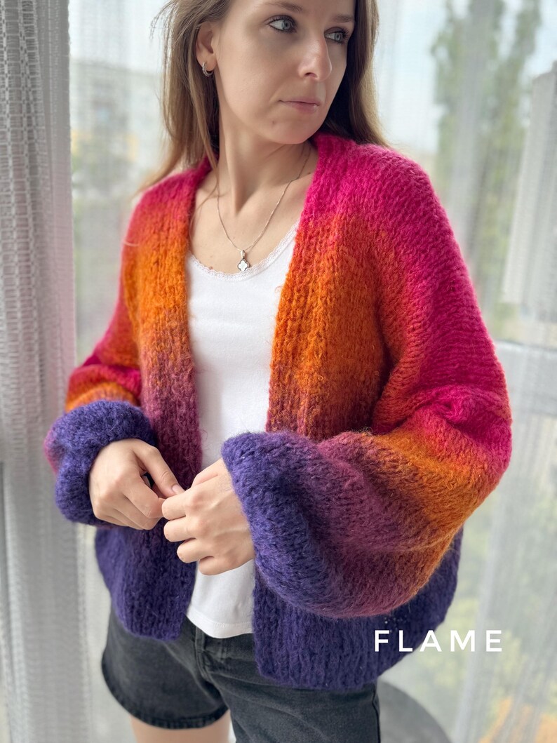 Puede incluir: Un c&aacute;rdigan de manga larga con un degradado de rosa, naranja y morado. El c&aacute;rdigan tiene un corte holgado y cuello en V. El texto "FLAME" es visible en la esquina inferior derecha de la imagen.