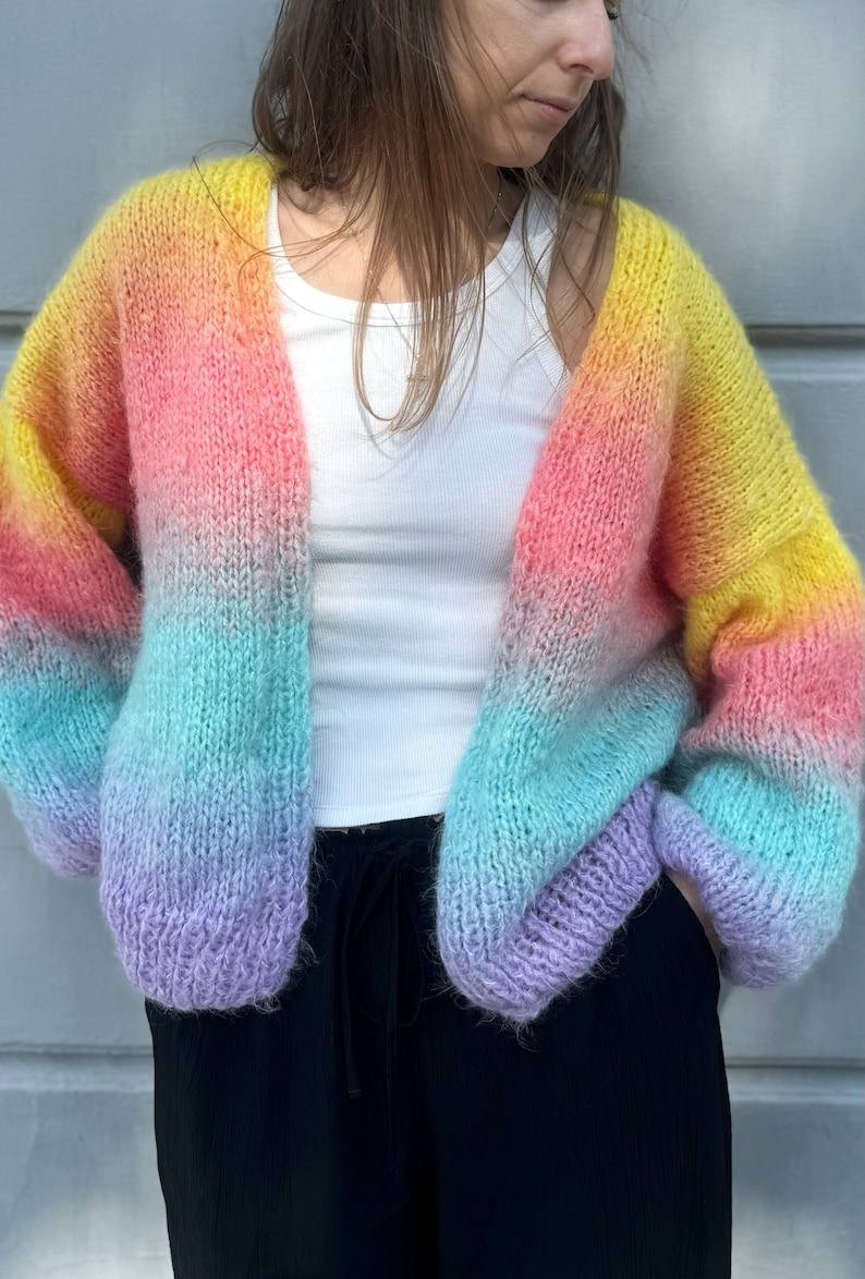 Puede incluir: Un c&aacute;rdigan de punto con un degradado de colores arco&iacute;ris, de corte holgado y mangas largas. El c&aacute;rdigan est&aacute; hecho de un hilo suave y peludo y tiene un estilo relajado y casual.