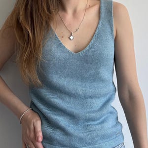 Puede incluir: Un top de punto azul claro sin mangas con escote en V. El top está hecho de una tela suave y ligera y tiene un ajuste holgado.