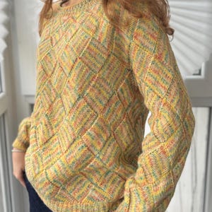 May include: A knitted jumper in a diamond pattern, featuring a crew neck and long sleeves. The colour scheme includes yellow, orange, green, and blue. The jumper is made from a soft, textured yarn. The garment is a warm, comfortable knit.