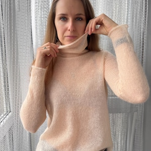 Pu&ograve; includere: Un maglione a maniche lunghe trasparente color pesca pallido con collo alto. Il capo &egrave; realizzato in un tessuto a maglia leggero e semitrasparente con una consistenza morbida e soffice, maniche lunghe e un orlo dritto.