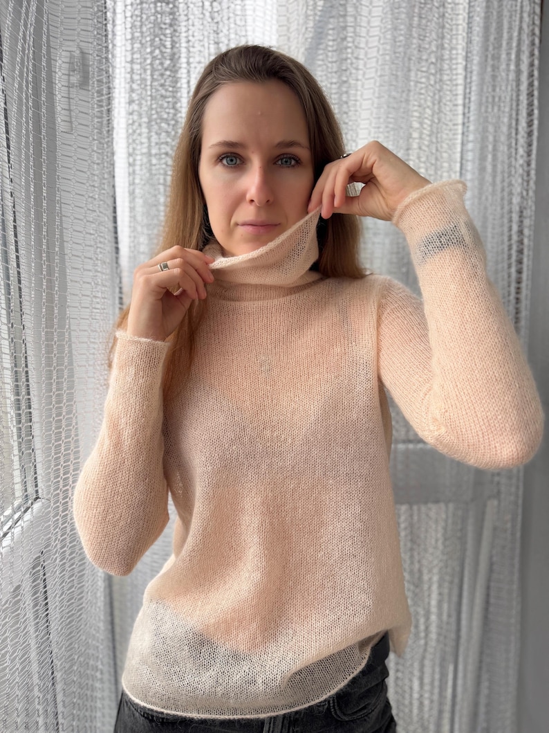 Pu&ograve; includere: Un maglione a maniche lunghe trasparente color pesca pallido con collo alto. Il capo &egrave; realizzato in un tessuto a maglia leggero e semitrasparente con una consistenza morbida e soffice, maniche lunghe e un orlo dritto.