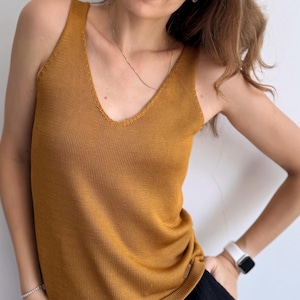May include: A mustard yellow sleeveless knitted tank top with a v-neck.