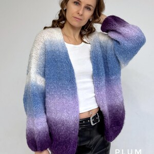 Puede incluir: Un c&aacute;rdigan de manga larga y abertura frontal con un patr&oacute;n de color degradado. El c&aacute;rdigan es blanco en la parte superior, pasando a azul claro, luego a morado y finalmente a morado oscuro en la parte inferior. El c&aacute;rdigan est&aacute; hecho de un hilo suave y esponjoso.