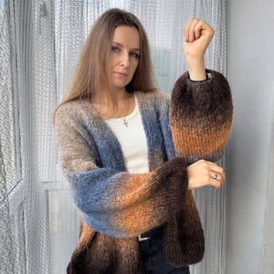 May include: A brown, blue, and orange ombre cardigan with long sleeves and a loose fit. The cardigan has a V-neck and is made of a soft, knitted fabric. The word "NIGHT" is printed in white letters at the bottom of the image.