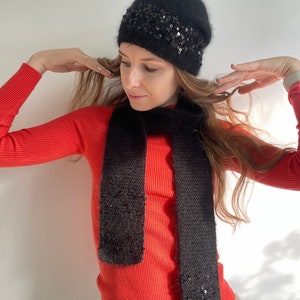 May include: A black fuzzy knit beanie with a band of sequins. The beanie is paired with a matching black fuzzy knit scarf.