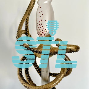 May include: A gold-colored octopus sculpture with a white and red speckled squid head on top of a silver sword. The sword has the text "MADE IN ITALY" on the blade.