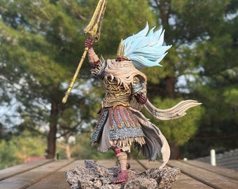 May include: A detailed figurine of The Nameless King, a character from a video game. The figure is posed on a rocky base, holding a golden spear aloft. It features intricate armor, flowing blue hair, and a tattered cape. The base reads "The Nameless King."