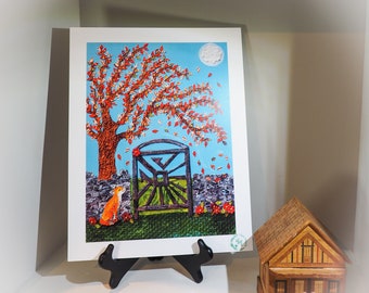 May include: An art print of a rural landscape featuring a fox, a tree with red leaves, and a gate. The artwork has a textured appearance, with a blue sky and a full moon. The print is displayed on a black easel.